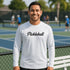 Man wearing a white 'Pickleball' shirt on a tennis court with other players in the background.